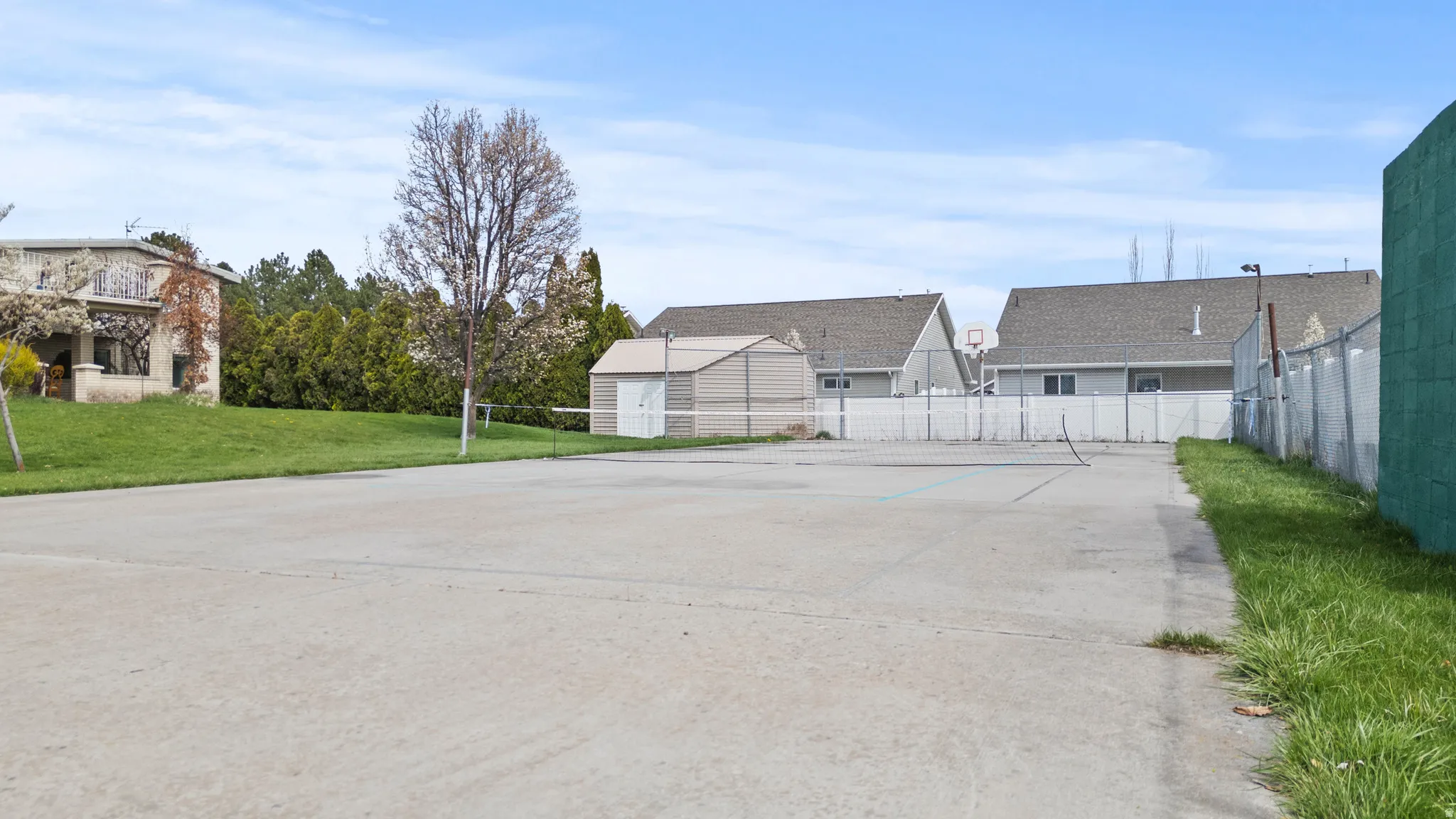 Concrete recreational court featuring a tennis net, basketball hoop, and a storage shed