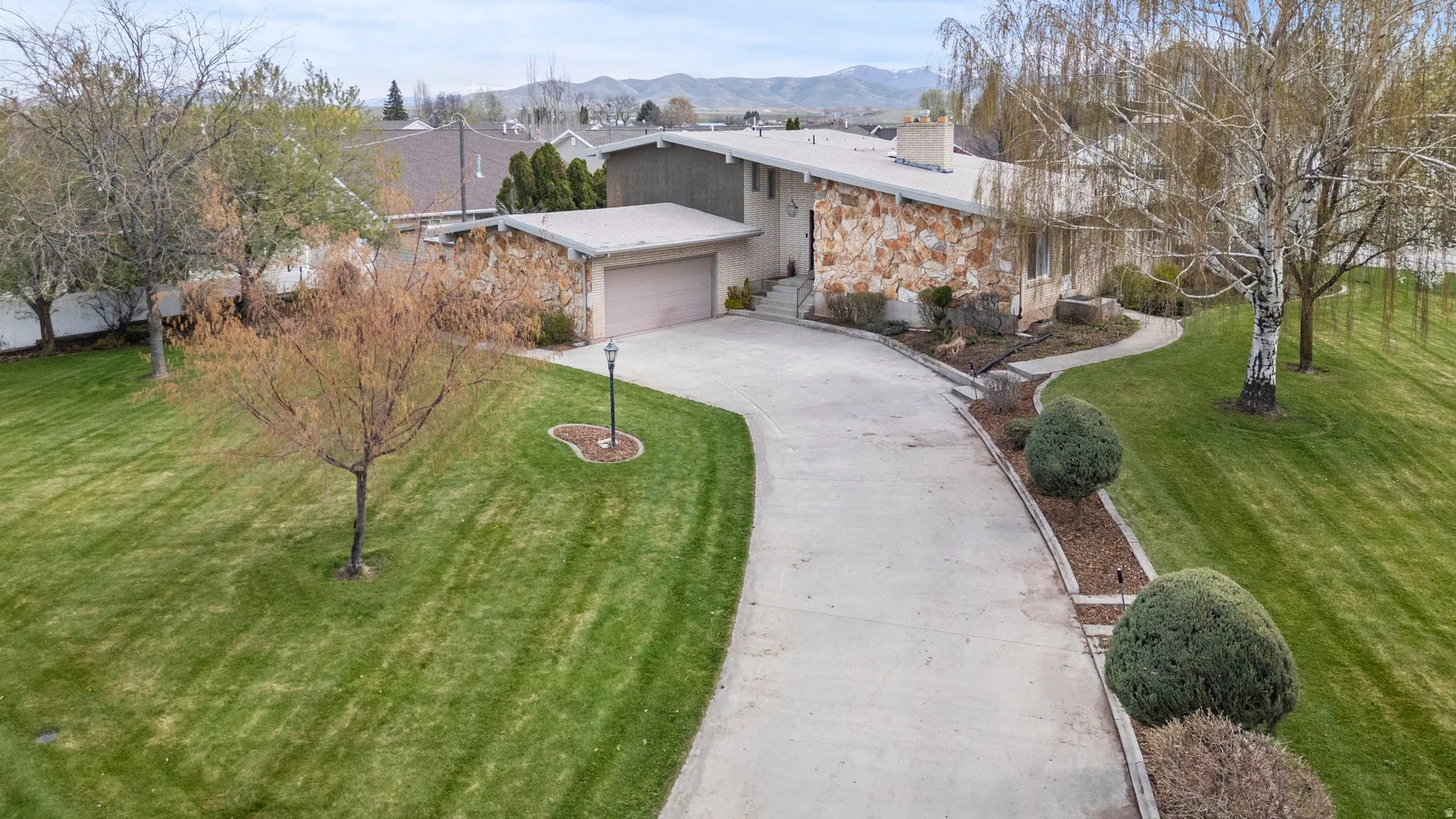 Mid-century modern residence featuring extensive stone veneer, a large two-car garage, and a concrete driveway