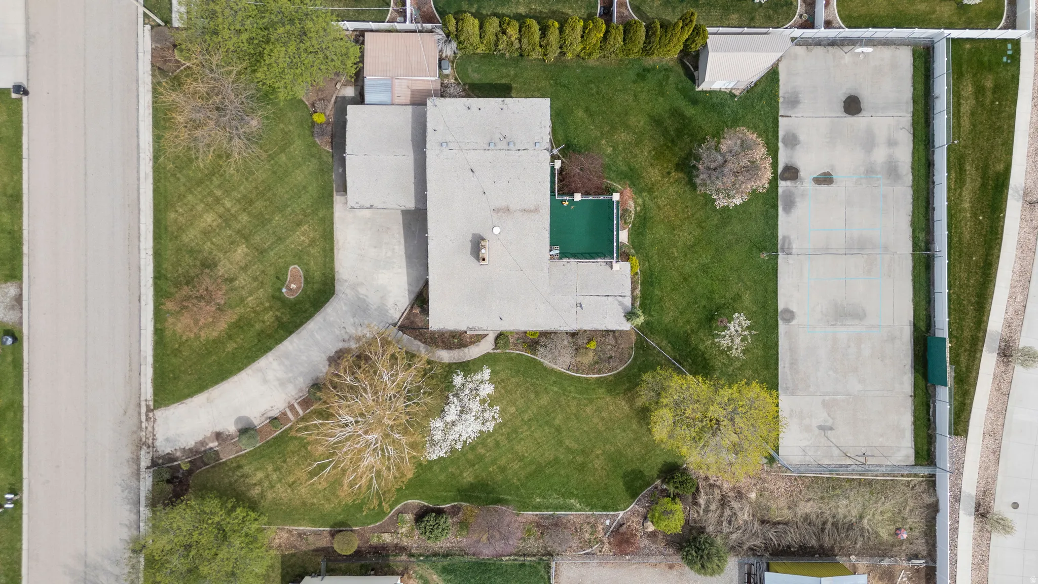 Expansive property featuring a curved driveway, large grassy areas, mature trees, an outdoor swimming pool, and a concrete court