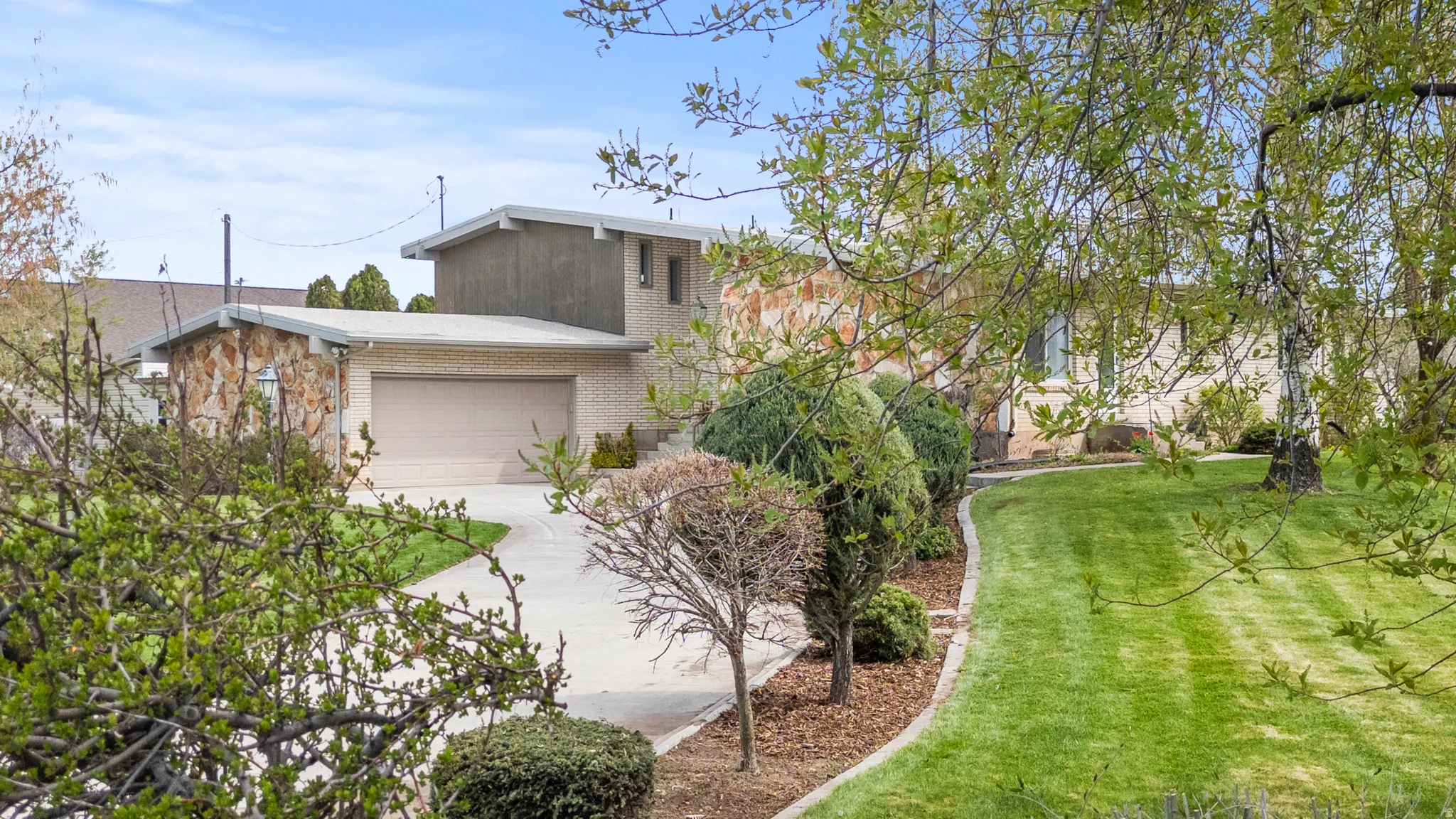 Mid-century modern residence featuring a dual garage, a concrete driveway, and natural stone and brick exterior accents