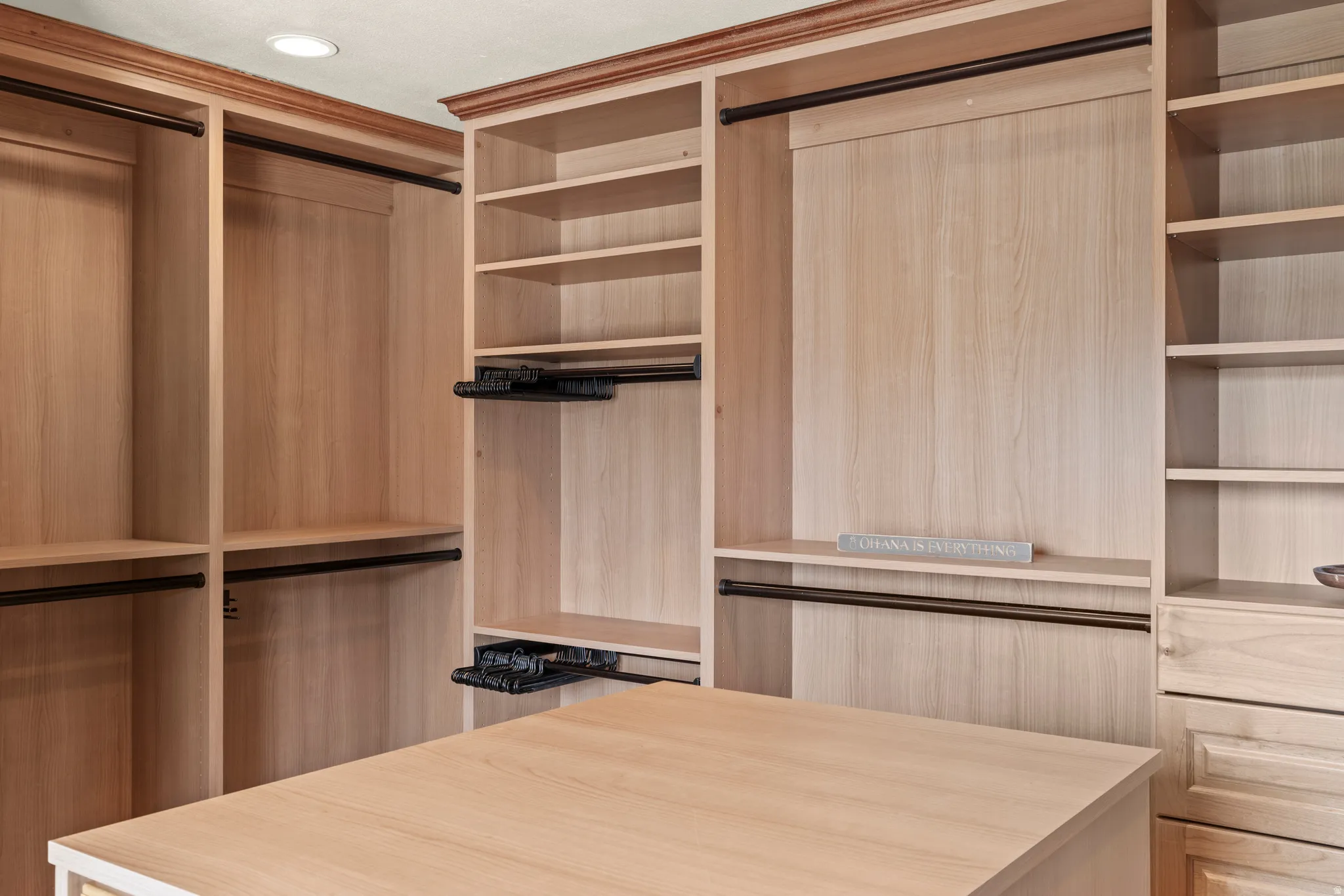 Built-in closet system featuring natural wood-finish cabinetry, extensive shelving, multiple hanging rods, and a central island with storage