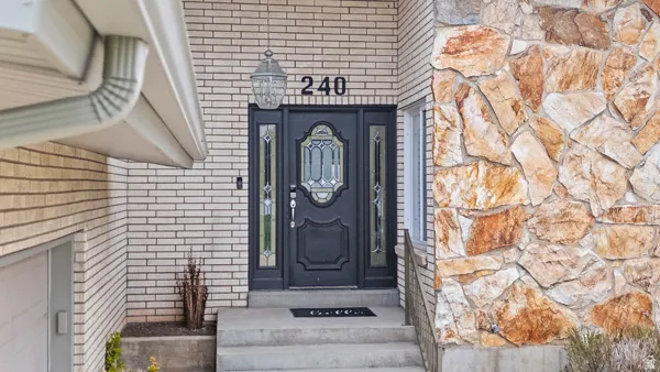 Welcoming entry featuring a striking black lacquered front door with decorative glass panels and sidelights, framed by contrasting brick and stone exterior finishes