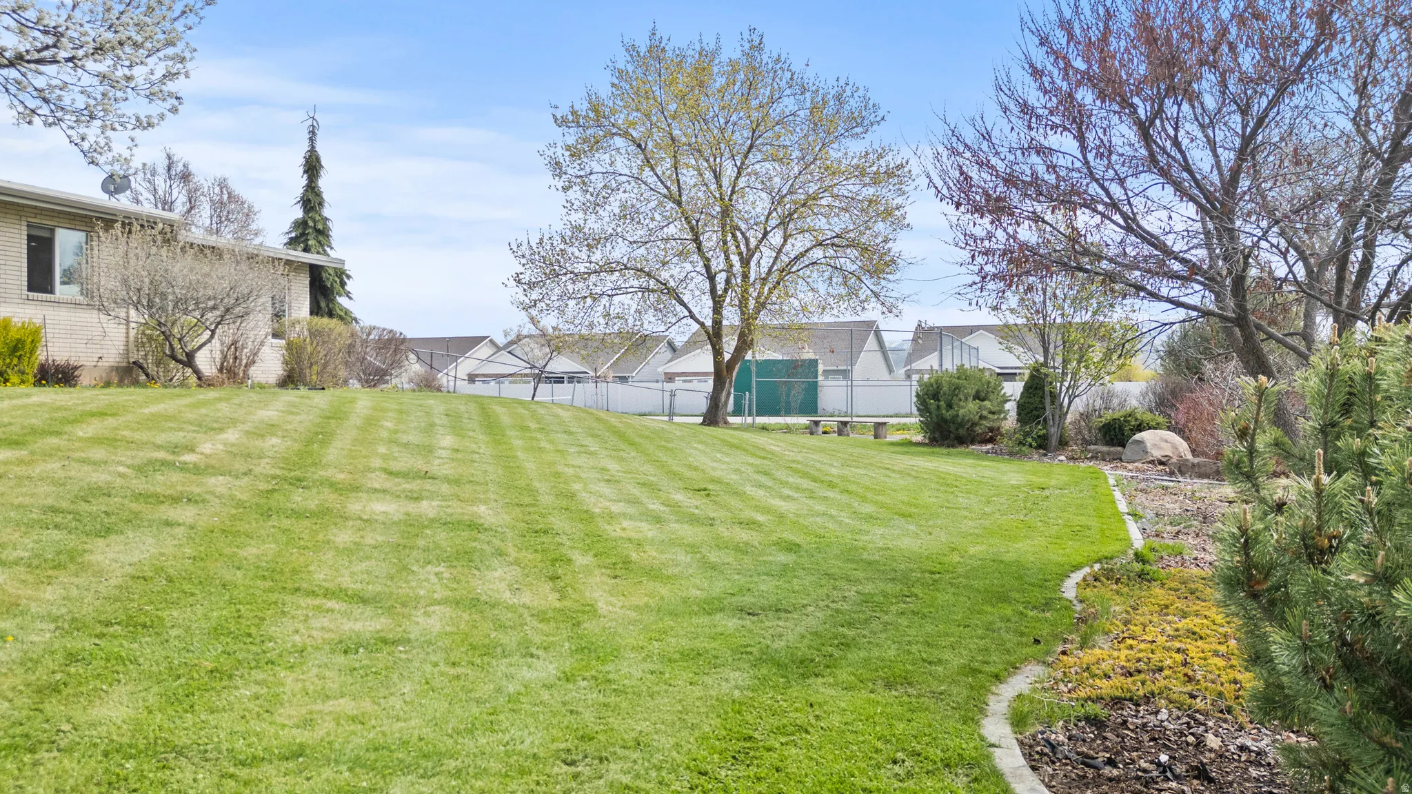 Expansive backyard featuring a lush green lawn, mature trees, and a decorative rock border