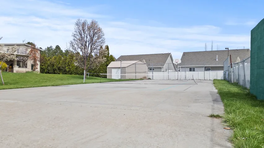 Concrete recreational court featuring a tennis net, basketball hoop, and a storage shed