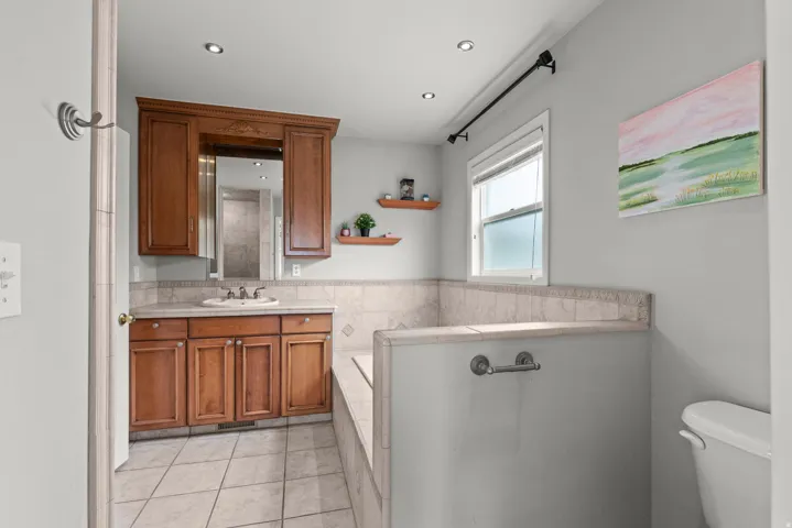 Spa-inspired master bathroom featuring rich wood-finish cabinetry with dual vanity, ceramic tile flooring, and a deep soaking tub