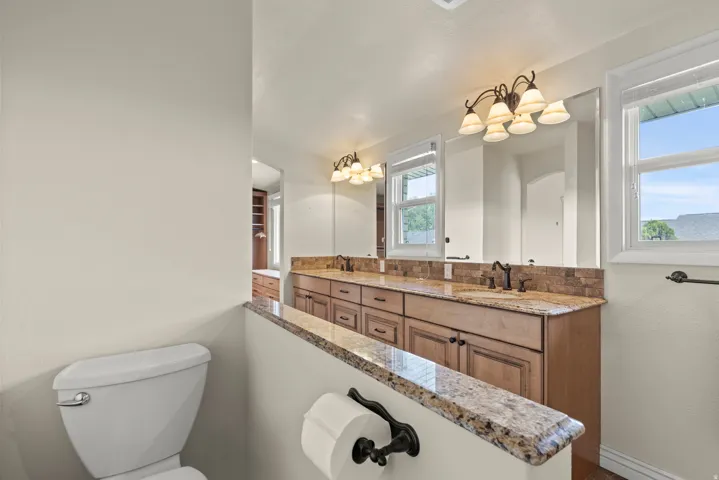 Spa-inspired primary bathroom showcasing a dual-sink vanity with warm wood cabinetry, granite countertops, and bronze-finished fixtures
