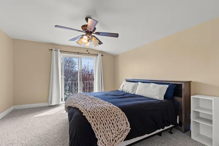 Spacious bedroom offering neutral wall tones, carpeted flooring, and abundant natural light from sliding glass doors opening to a balcony