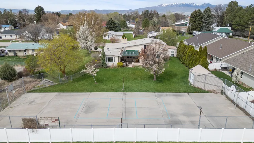 Expansive outdoor recreational space featuring a professionally surfaced tennis court with regulation markings, bordered by white fencing