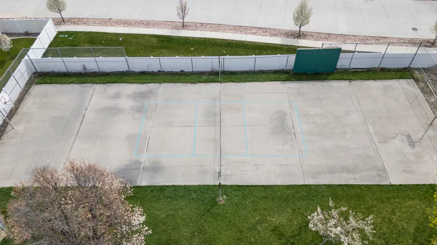 Expansive outdoor recreational space featuring a concrete court area with marked sections, bordered by manicured lawn and mature landscaping