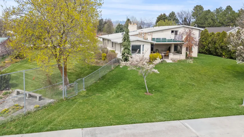 Expansive front lawn with mature trees and a chain-link fence