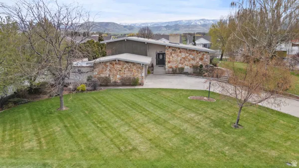Modern residence featuring a striking stone and stucco exterior with clean architectural lines, positioned on a generous manicured lawn with mature landscaping