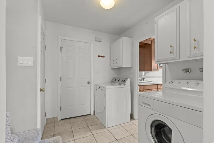 Laundry room featuring side-by-side washer and dryer units, white cabinetry with brass hardware, tile flooring, and ample counter space
