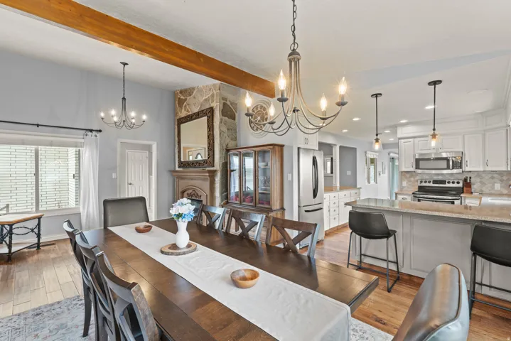 Open-concept dining and kitchen featuring a wood-finish table with seating for eight, stainless steel appliances, white cabinetry with quartz countertops, a large center island with bar seating, exposed wood ceiling beams, pendant lighting, and hardwood f