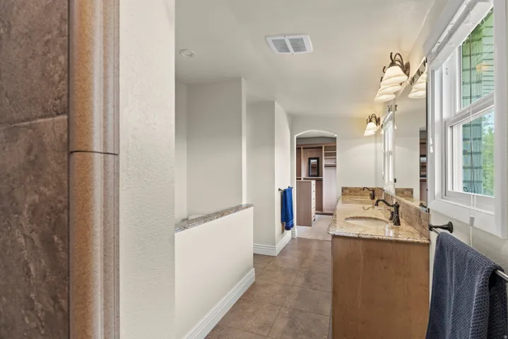 Spacious bathroom featuring a dual vanity with light stone countertops, integrated sinks, and bronze-finish fixtures