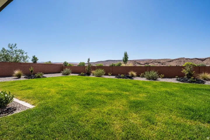 Expansive lawn area with a brick perimeter wall, gravel landscaping, established shrubbery, and distant desert hills