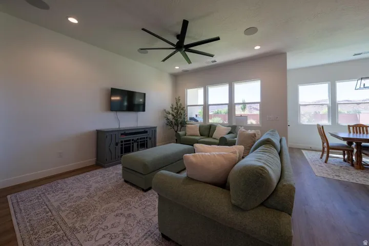 Spacious living room featuring hardwood flooring, a ceiling fan with integrated lighting, and a wall-mounted flat-screen television