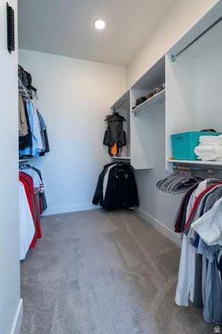 Walk-in closet featuring built-in shelving, multiple hanging rods, recessed ceiling lighting, and light grey carpeting