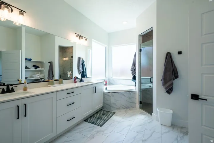 Spa-inspired primary bathroom featuring dual vanities with ample storage, marble-look tile flooring, and a freestanding soaking tub