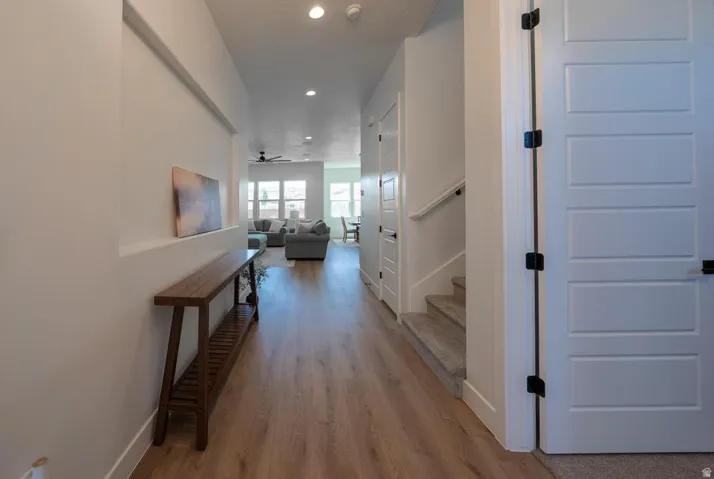 Bright, open hallway showcasing refinished wood-finish flooring, recessed ceiling lighting, and clean white walls with substantial baseboards