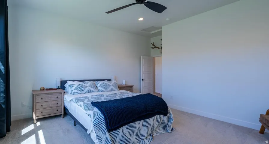Spacious primary bedroom featuring neutral wall finishes, carpeted flooring, ceiling fan with recessed lighting, and an ensuite entry