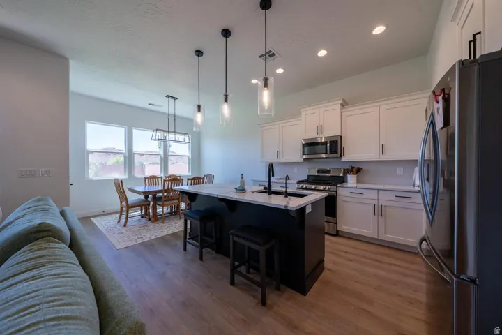 Open-concept kitchen and dining area featuring a dark-toned island with seating, pendant lighting, stainless steel appliances, and white cabinetry