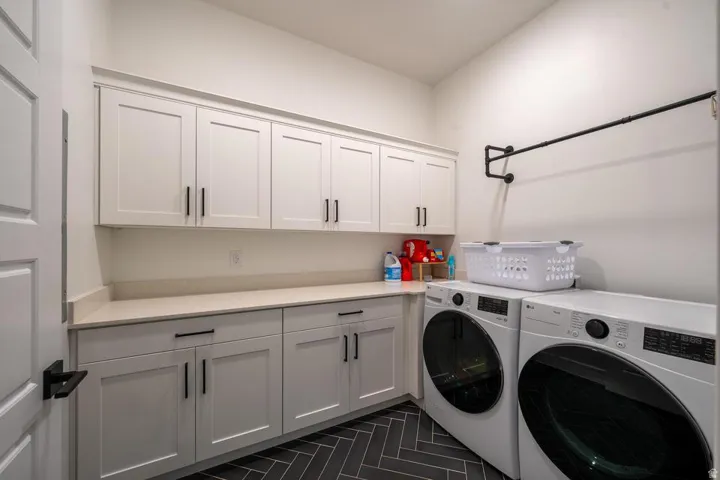 Laundry room featuring extensive white shaker cabinetry, light-toned countertops, and dark herringbone floor tiling