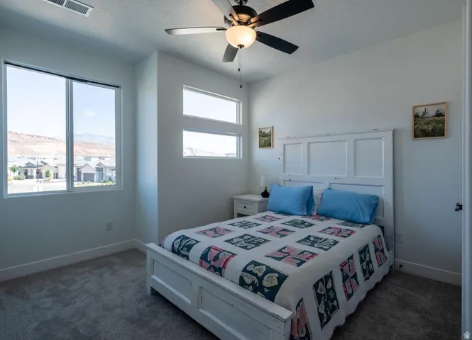 Bright room featuring a large window, two transom windows, gray carpet, and a ceiling fan with light fixture