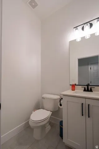 Modern bathroom featuring a white vanity cabinet with black hardware and countertop, vessel sink, matte black faucet, and integrated mirror with illuminated vanity lighting