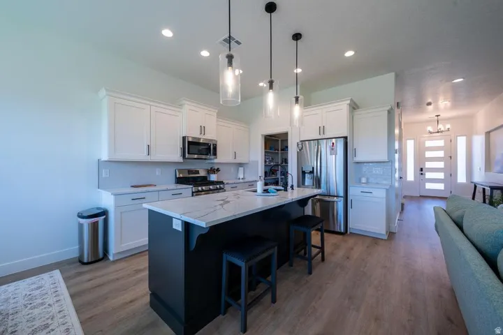 Kitchen featuring an oversized island with seating, white shaker-style cabinetry, stainless steel appliances, and wood-finish flooring