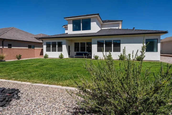 Modern two-story residence featuring a clean-lined white exterior with dark roof accents, expansive rear lawn with mature landscaping, multiple large windows providing natural light, contemporary architectural design with geometric roofline, and professio