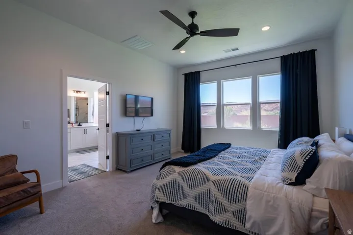 Spacious primary bedroom featuring dual beds, soft carpet flooring, and a ceiling fan with recessed lighting