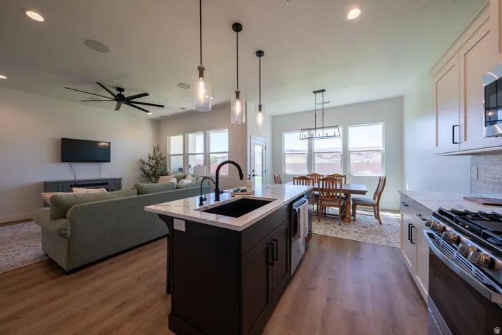 Open-concept kitchen and living area featuring a center island with waterfall countertop edge and prep sink, stainless steel appliances including a professional-style range, white cabinetry with soft-close hardware, pendant lighting over the island, wood-