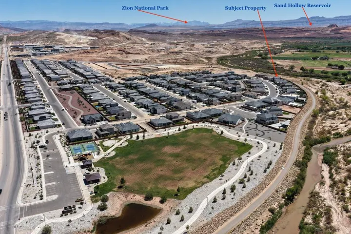 Aerial view of a master-planned community featuring expansive residential development with organized street layouts, central green space with manicured landscaping, perimeter pathways, and proximity to regional landmarks including Zion National Park and S
