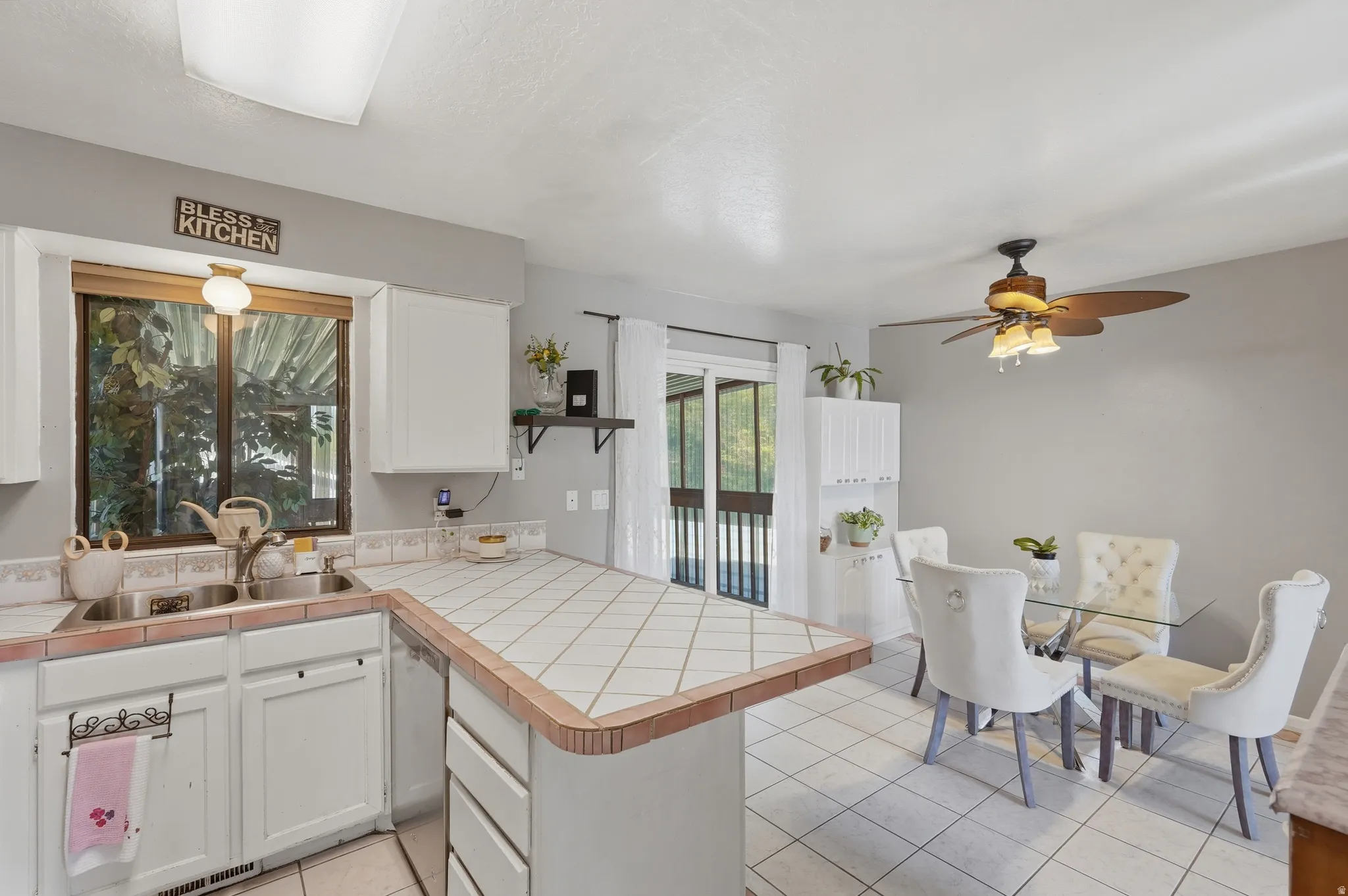 Bright, open kitchen and dining area featuring white cabinetry, tile countertops with wood-finish edging, stainless steel appliances, and a centered island with additional workspace