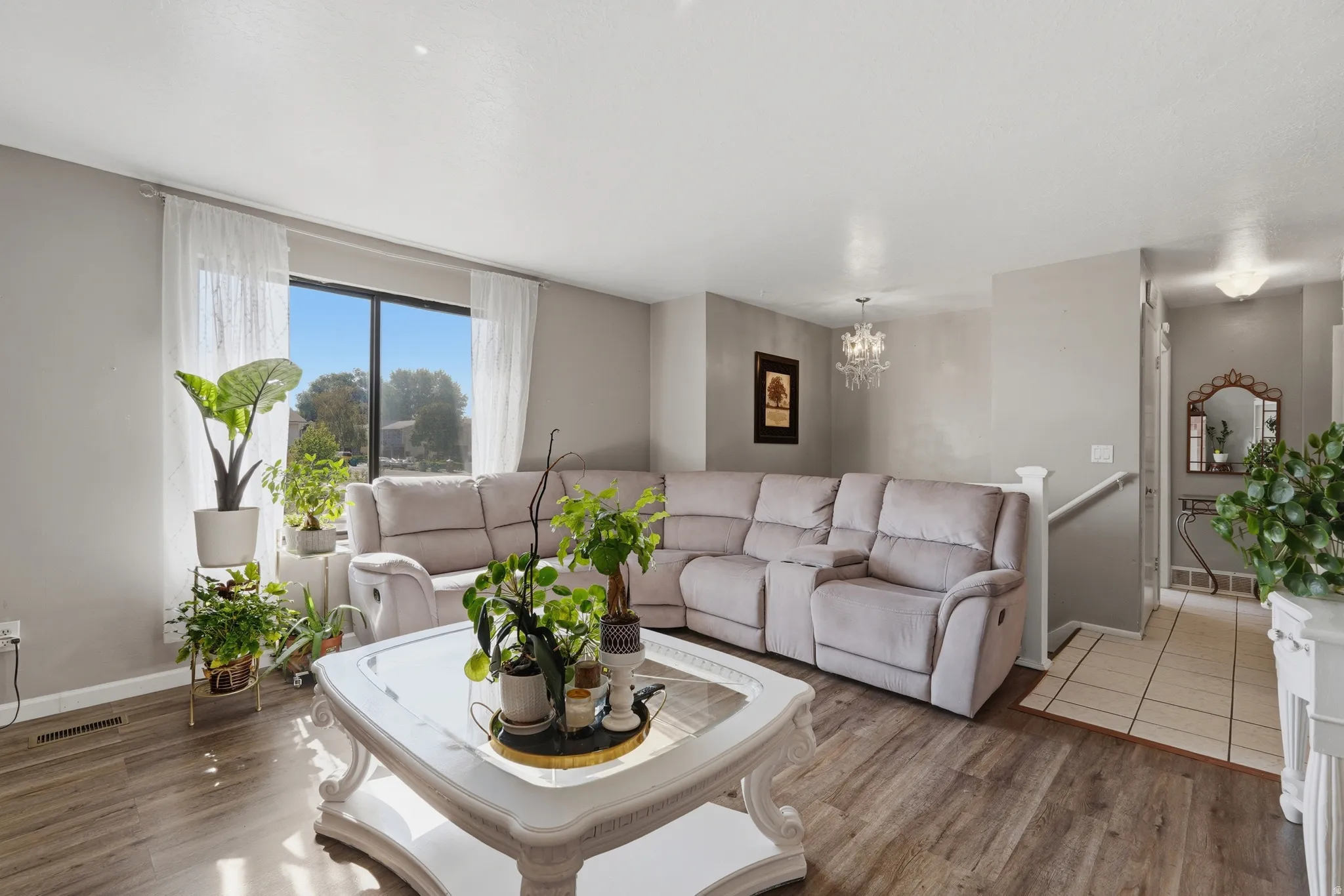 Bright and spacious living room featuring a sectional sofa arrangement, wood-finish flooring throughout, and abundant natural light from large windows