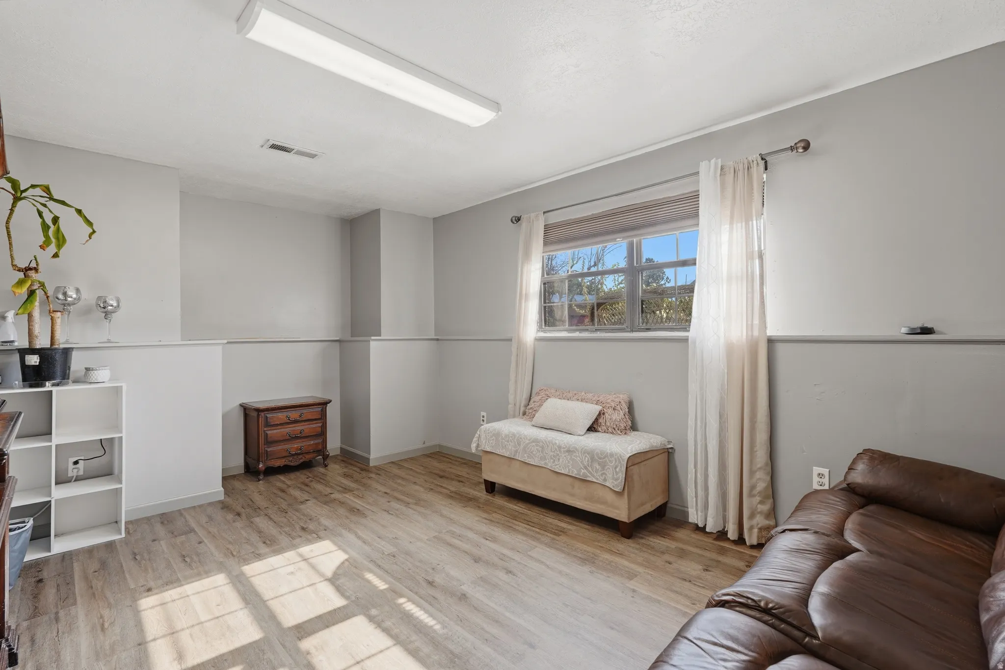 Bright room featuring light wood-finish flooring, neutral gray walls with wainscoting, and a window with natural light