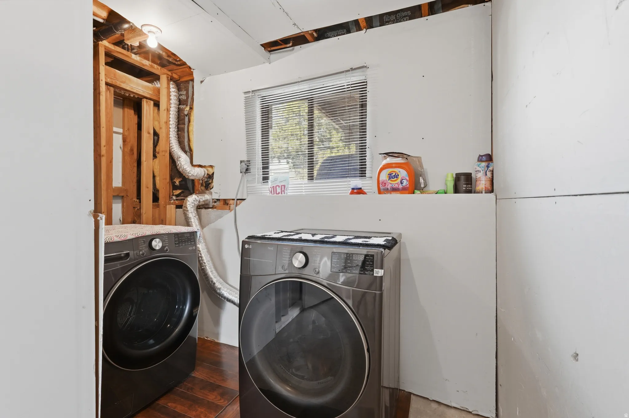 Laundry area featuring wood-finish flooring, a window with blinds, and exposed ceiling joists
