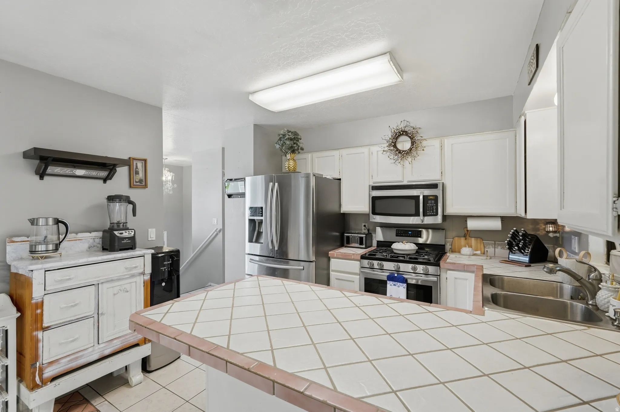 Kitchen featuring white cabinetry, stainless steel appliances, a tiled island countertop, and a double basin sink
