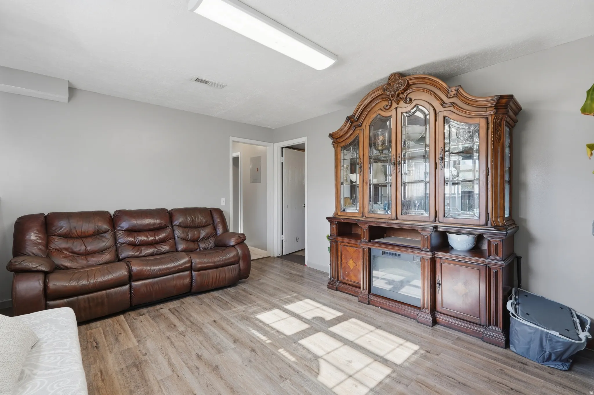 Spacious living area showcasing a reclining leather sectional sofa, wood-finish flooring throughout, and an elegant wooden display cabinet with glass doors and lower storage