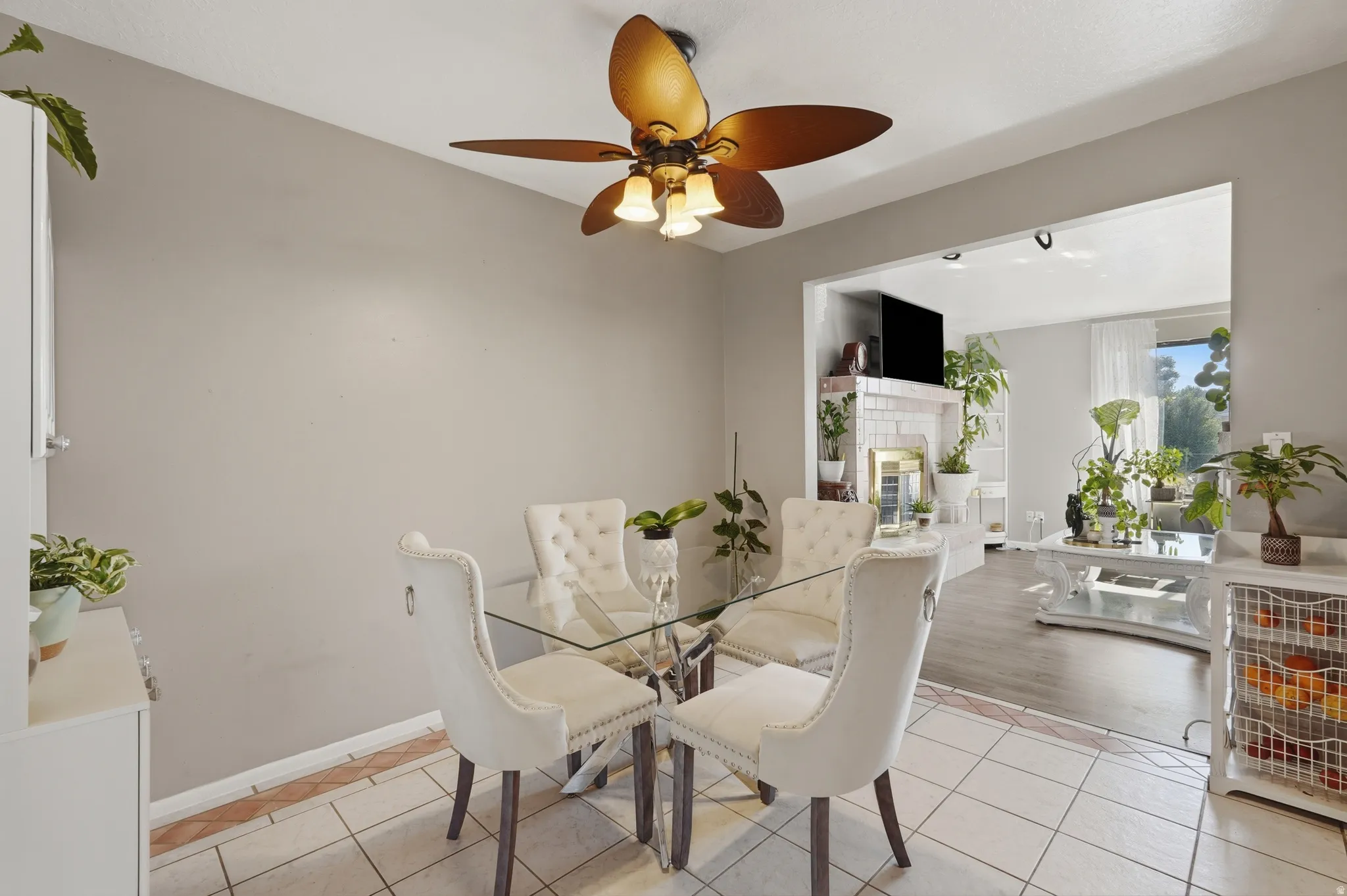 Bright dining area featuring a glass-top table with metal base, upholstered dining chairs, ceramic tile flooring, and abundant natural light from adjacent windows