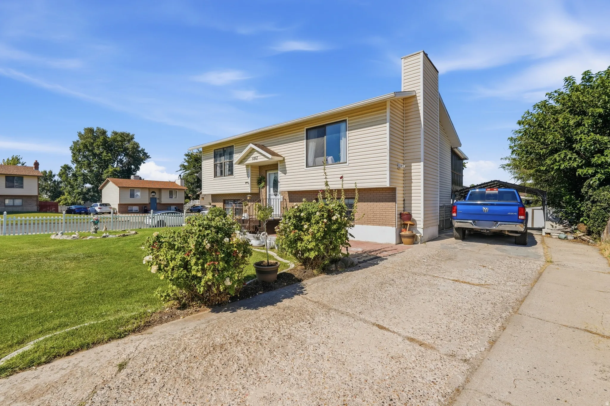 Split-level home featuring a spacious front elevation with cream and tan exterior siding, peaked roofline with architectural detailing, and a welcoming covered entry