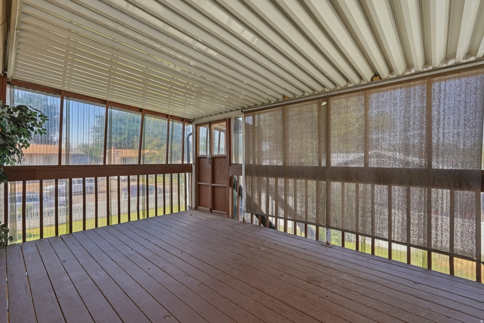 Screened porch featuring wood-finish flooring, a metal ceiling, and roll-down sun shades