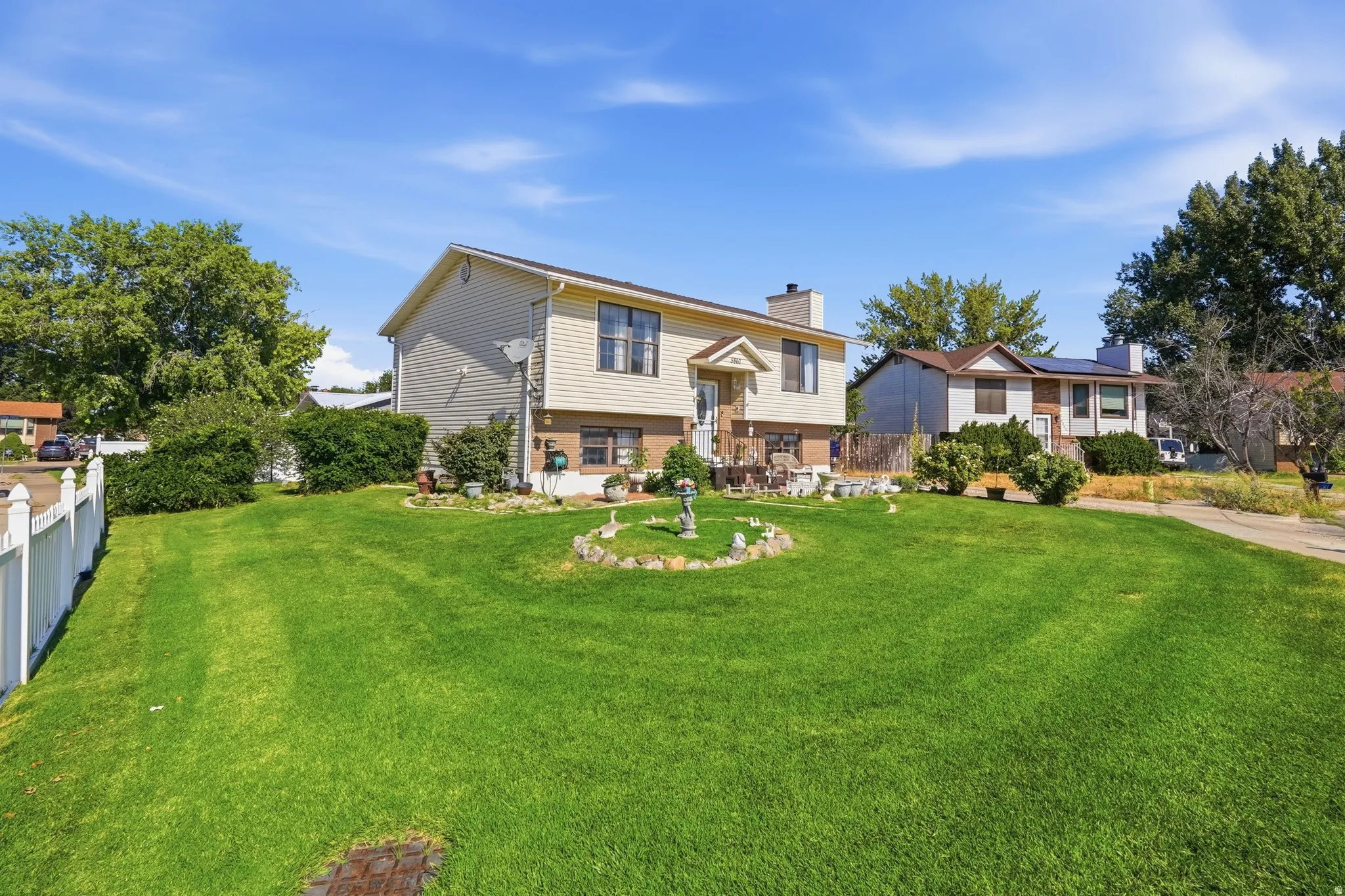 Spacious residential lot featuring a two-story home with mixed siding exterior, covered front porch, and manicured lawn with mature landscaping and ornamental plantings
