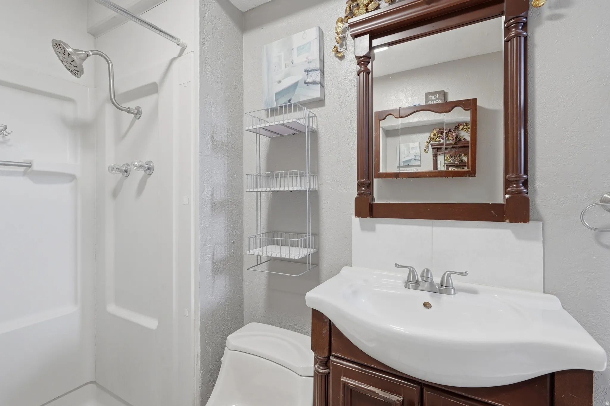 Bathroom featuring a white shower with a chrome showerhead, a white toilet, and a vanity with a white basin sink and brown cabinetry