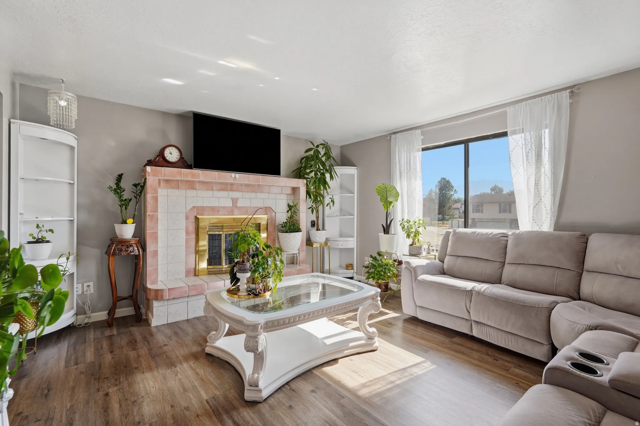 Living area featuring a tiled fireplace with a brass firebox, wood-finish flooring, and a large window
