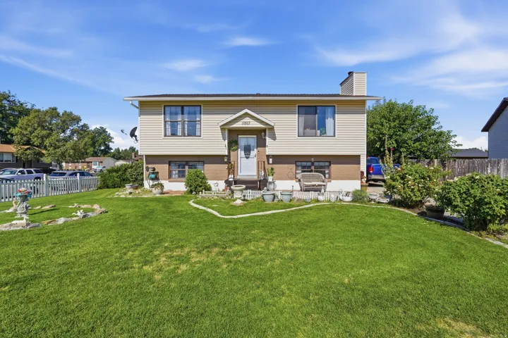 Charming split-level home featuring cream-colored vinyl siding, a gabled roofline with chimney, and multi-pane double-hung windows