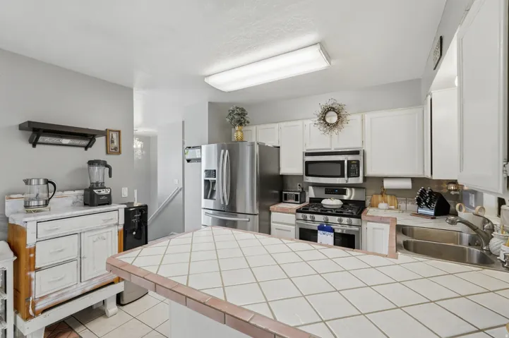 Kitchen featuring white cabinetry, stainless steel appliances, a tiled island countertop, and a double basin sink