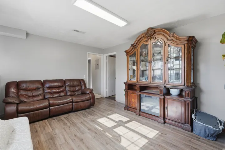Spacious living area showcasing a reclining leather sectional sofa, wood-finish flooring throughout, and an elegant wooden display cabinet with glass doors and lower storage