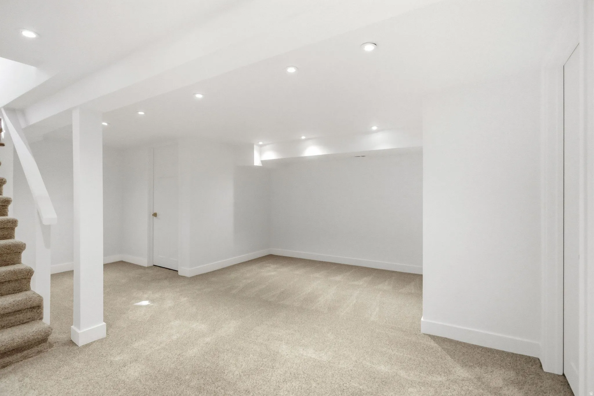 Finished basement featuring open layout with neutral carpet flooring, recessed ceiling lighting, white drywall construction, and structural support columns