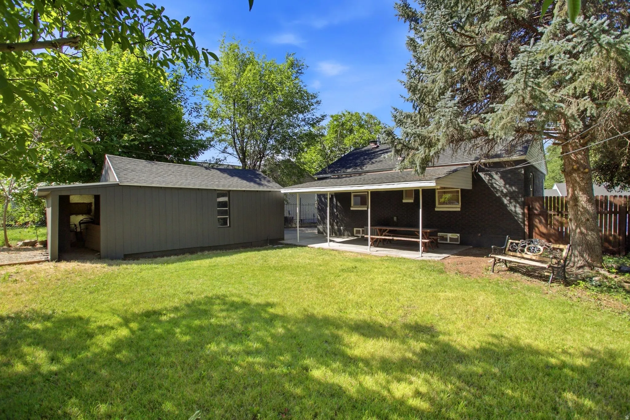 Spacious backyard featuring a manicured lawn, dedicated storage shed, covered patio area, and mature trees